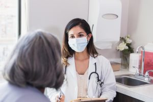 A mid adult female doctor has a serious discussion with a senior female patient. The doctor is wearing a protective face mask.